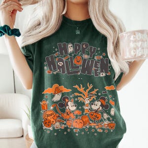Puede incluir: Camiseta verde oscuro con un dise&ntilde;o de Halloween. El dise&ntilde;o presenta el texto "Happy Halloween" con personajes de dibujos animados, calabazas, fantasmas y caramelos. La camiseta tiene un corte holgado.