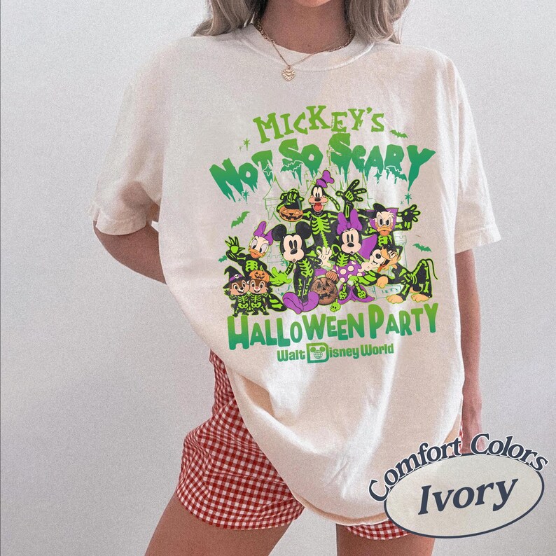 Op de afbeelding: Ivoor kleurig T-shirt met een Halloween-thema met Mickey Mouse en vrienden. Het ontwerp bevat de tekst "Mickey's Not So Scary Halloween Party" en "Walt Disney World" in het groen. Het shirt is van het merk Comfort Colors.