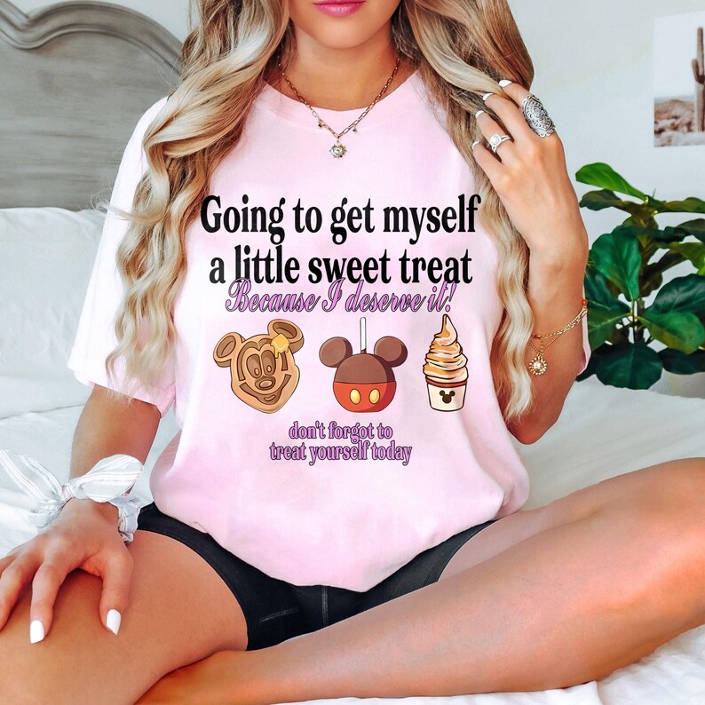 Puede incluir: Camiseta rosa claro con el texto "Going to get myself a little sweet treat Because I deserve it!" e ilustraciones de un gofre de Mickey Mouse, una manzana de caramelo de Mickey Mouse y un helado. Tambi&eacute;n se incluye el texto "don't forget to treat yourself today".