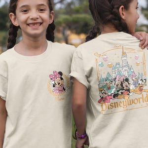 May include: Two children wearing cream colored t-shirts with a Disney World theme. One shirt features Mickey Mouse and Minnie Mouse, the other shirt features Mickey Mouse, Minnie Mouse, Donald Duck, Goofy, Pluto, and a castle with the text "Disneyworld 1971 - ".