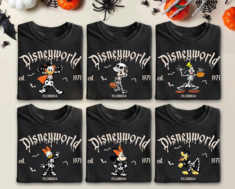 Op de afbeelding: Zes zwarte t-shirts met Halloween-thema Disney-personage-ontwerpen. Elk shirt heeft een ander personage in skeletvorm, met de tekst "Disneyworld" en "Florida 1971". Decoratieve pompoenen, spinnen en vleermuizen omringen de shirts.