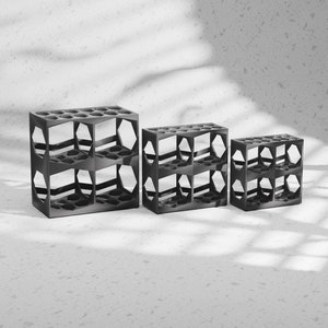 May include: Three black metal storage shelves of different sizes. The shelves are made of a grid pattern and are designed to hold small items.