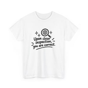 May include: A white short-sleeve t-shirt featuring a black graphic of a magnifying glass over a spiral icon, surrounded by small star shapes, with the text "Upon closer inspection, you are correct." printed in black below the graphic.