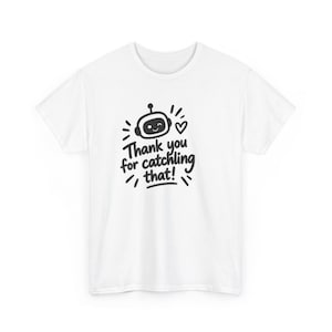 May include: A white short-sleeved t-shirt featuring a black graphic of a smiling robot head, a small heart, and the text "Thank you for catching that!" centred on the chest. The design includes small radiating lines around the robot head.