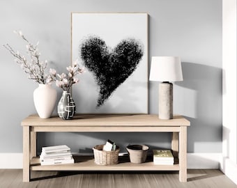 May include: A light wood console table with two shelves. The top shelf has a black and white print of a heart, a white lamp with a white shade, and two white vases with flowers. The bottom shelf has books, a wicker basket, and a woven basket.