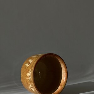 May include: A brown ceramic planter with a white design. The planter is empty and sitting on a white surface.