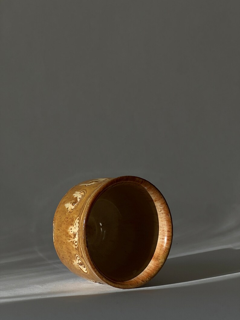 May include: A brown ceramic planter with a white design. The planter is empty and sitting on a white surface.