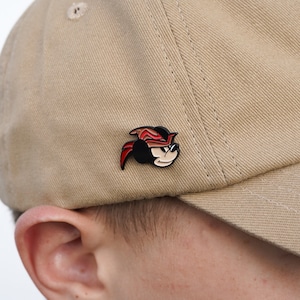 May include: A tan baseball cap with a black and red enamel pin of Mickey Mouse wearing a red bandana.