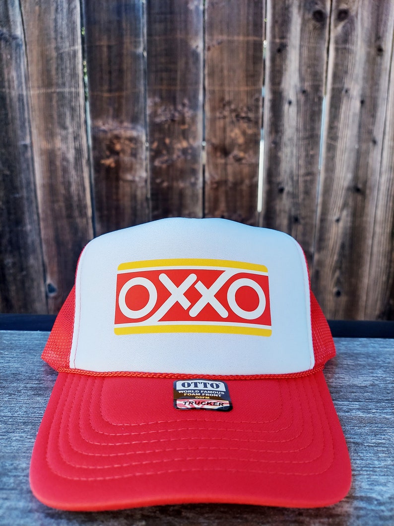 Op de afbeelding: Rode en witte truckercap met een geel en rood "OXXO" logo op de voorkant. De cap heeft een zwart "OTTO WORLD FAMOUS FOOD MART" label aan de zijkant.
