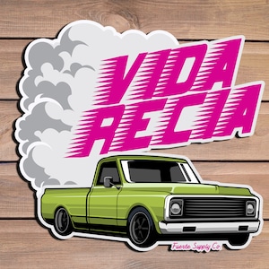 May include: A green pickup truck with a white cloud of smoke behind it. The truck has a pink graphic that says "Vida Rica" with a white outline. The graphic is stylized with a speed line effect. The truck has a black grill and black wheels. The text "Fuerte Supply Co." is at the bottom of the image.