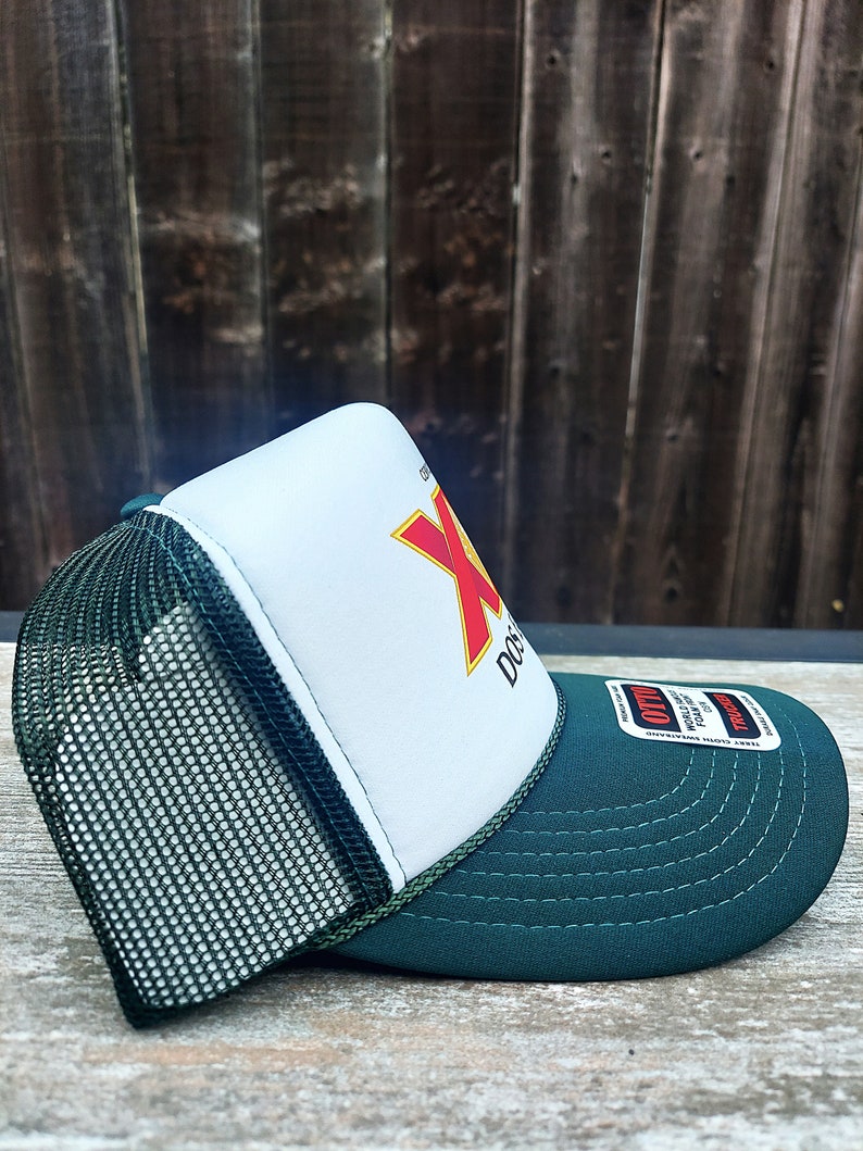 May include: A green and white trucker hat with a red and yellow logo that says "Dos Equis" on the front. The hat has a mesh back and a green brim.