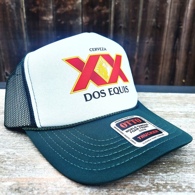 May include: A white and green trucker hat with a black mesh back. The front of the hat features a red and yellow logo that says "Cerveza XX Dos Equis". The back of the hat has a black label that says "Otto World Famous Foam Front OSFM Trucker Durable Snap Closure".