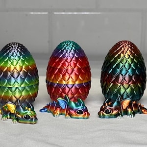 May include: Seven decorative dragon eggs in a row, each with a baby dragon. The eggs are in a range of colours, including pearlescent white, rainbow, and black. The eggs have a textured, scaled appearance.