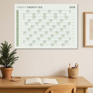May include: A 2026 wall calendar in light green and white, with the text "TWENTY TWENTY-SIX" at the top. The calendar grid is displayed, with months listed vertically on the left. The calendar is displayed on a wall.