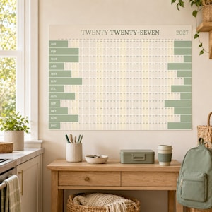 May include: A wall calendar for the year 2027 with the text TWENTY TWENTY-SEVEN at the top. The calendar features a grid layout with months listed on the left in sage green and white, with alternating light green and cream columns for the days.