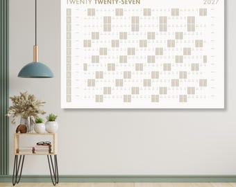 Puede incluir: Un calendario de pared rectangular grande para el año 2027, con un diseño minimalista. El calendario presenta un diseño de cuadrícula con casillas de color beige sobre un fondo blanco. El texto "TWENTY TWENTY-SEVEN" y el año están impresos en dorado apagado.