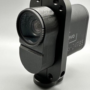 Puede incluir: Una cámara de acción negra con una cubierta de lente y un soporte de montaje. La cámara tiene el texto "evo" y "b-24T85" impreso en el lateral.