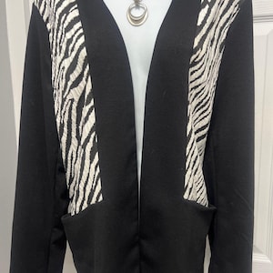 May include: Black open-front blazer with zebra print panels and two front pockets. The zebra print is white and tan. A silver necklace with a double-circle pendant is visible.