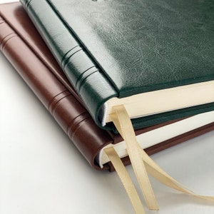 Op de afbeelding: Twee lederen notitieboeken, &eacute;&eacute;n bruin en &eacute;&eacute;n groen, zijn schuin op elkaar gestapeld. Elk notitieboek heeft een lint als bladwijzer. De covers hebben een textuur. De pagina's zijn cr&egrave;mekleurig.