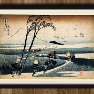 Pode incluir: Uma gravura japonesa em madeira vintage que retrata uma cena de pessoas caminhando por um caminho com o Monte Fuji ao fundo. A gravura é em tons de azul, marrom e branco, com alguns acentos vermelhos. O céu está cheio de pedaços de papel branco que são levados pelo vento.