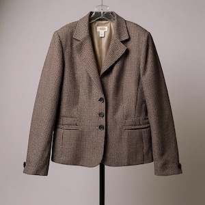 May include: A brown and black patterned blazer with a notched collar, three-button closure, and two front pockets. The blazer is hanging on a hanger. The lining is a light tan color.