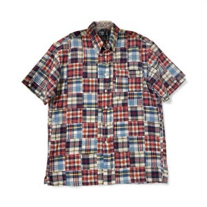 May include: Short-sleeved button-down shirt with a patchwork design. The shirt features a mix of red, blue, and white plaid patterns. The shirt has a collared neckline and a button-up front.