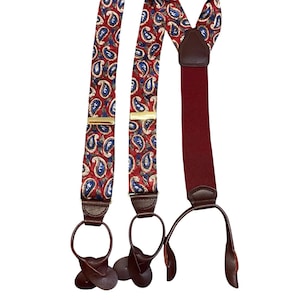 Puede incluir: Tirantes con estampado de cachemira con fondo rojo, detalles en azul y blanco y detalles en cuero marrón. Los tirantes tienen cierres metálicos dorados y presillas de cuero marrón.