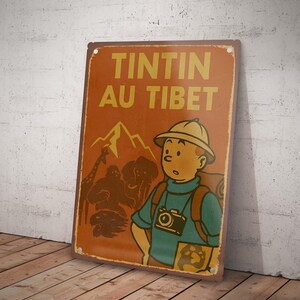 May include: A vintage-style metal sign featuring the text "TINTIN AU TIBET" in yellow letters on an orange background. The sign depicts a cartoon character with a camera, mountains, and animals. The sign is leaning against a wall.
