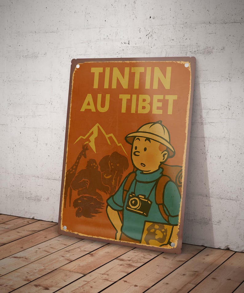 May include: A vintage-style metal sign featuring the text "TINTIN AU TIBET" in yellow letters on an orange background. The sign depicts a cartoon character with a camera, mountains, and animals. The sign is leaning against a wall.
