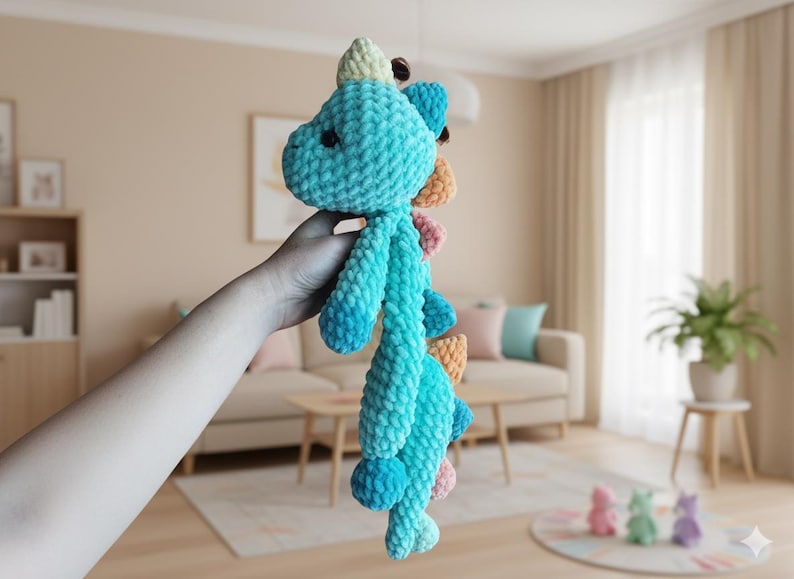 May include: A handmade, plush turquoise dinosaur toy with a light blue belly and colorful spines. The dinosaur is held up in front of a neutral background. The toy is made of soft, textured yarn.