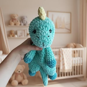 May include: A handmade turquoise crochet dinosaur plush toy with a light yellow horn. The dinosaur has dark blue accents on its feet and tail. The toy is soft and cuddly, perfect for a child's nursery or playroom.