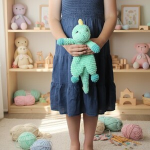 May include: A child holds a handmade, turquoise crochet dinosaur toy with blue accents. The background features a wooden shelf filled with other crochet toys, yarn, and wooden blocks. The scene suggests a craft or children's theme.