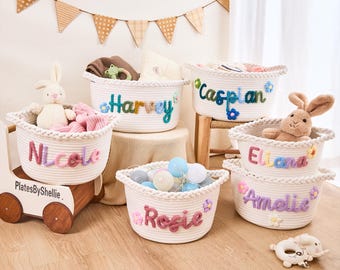 Puede incluir: Una colección de cestas de cuerda blancas, cada una con un nombre bordado en hilo colorido. Las cestas están llenas de juguetes y artículos para bebés. Los nombres incluyen Nicole, Harvey, Caspian, Eliana, Amelie y Rosie. También hay un vagón de juguete de madera.