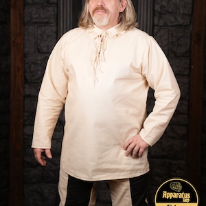 Pode incluir: Uma camisa de manga comprida de cor creme com um decote de renda. A camisa é feita de um tecido leve e tem um caimento solto.