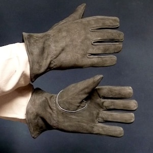 Puede incluir: Un par de guantes de ante gris oscuro. Los guantes se muestran con los dedos extendidos, mostrando las costuras y el diseño. Los guantes tienen un acabado suave y mate, adecuados para el frío o el trabajo.
