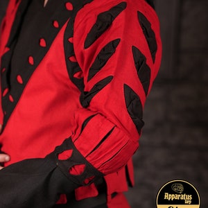 Pode incluir: Uma camisa de manga comprida vermelha e preta com um design único que apresenta recortes e detalhes em tecido preto. A camisa tem um decote alto e uma silhueta ajustada.
