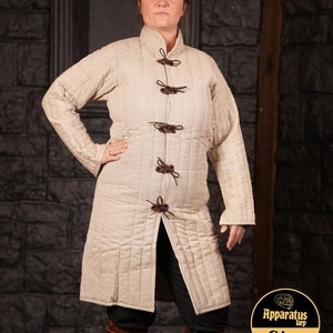 Puede incluir: Una chaqueta larga acolchada de color beige con lazos de cuero marrón. La chaqueta tiene un cuello alto y una abertura frontal con una cremallera larga. La chaqueta está hecha de una tela gruesa y duradera, perfecta para el clima frío.