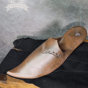 Könnte beinhalten: Ein brauner Lederschuh mit spitzer Zehenpartie und einem dekorativen Stichdetail. Der Schuh besteht aus einem einzigen Stück Leder und hat ein schlichtes Design.