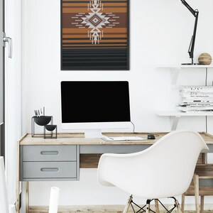 May include: A framed wall art print featuring a geometric design in shades of brown, white, and gray, set against a backdrop of horizontal black and brown stripes. The artwork hangs above a wooden desk with a computer and a white chair.
