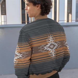 May include: A gray and brown patterned bomber jacket with a geometric design on the back and sleeves. The jacket features horizontal stripes and a brown collar and cuffs. The jacket is worn by a person.