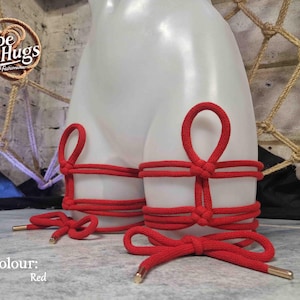 May include: Red rope bondage accessories are displayed on a white mannequin. The accessories include leg restraints and decorative bows. The text "Rope Hugs" is visible in the upper left corner, with the word "Red" below it.