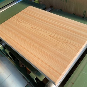 May include: A light brown wooden board with a smooth surface and visible grain patterns. The board is being processed on a large industrial machine.