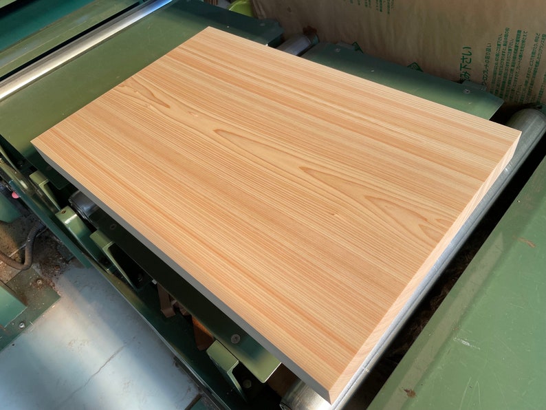 May include: A light brown wooden board with a smooth surface and visible grain patterns. The board is being processed on a large industrial machine.