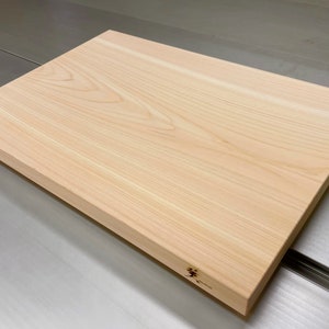 Puede incluir: Una tabla de cortar de madera grande, rectangular, hecha de madera clara con un patrón de veta natural. La tabla tiene un borde ligeramente redondeado y una superficie lisa. La tabla está sobre una superficie plateada.