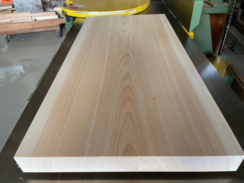 May include: A large, light-colored wood plank with a smooth surface and visible grain patterns. The plank is lying flat on a dark surface.