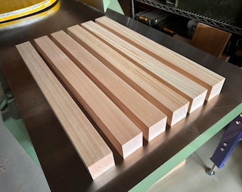 May include: Six wooden planks, all the same size and shape, are laid out on a metal surface. The planks are light brown in color and have a smooth, polished finish.
