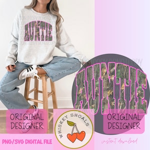 Peut inclure: Un sweat-shirt gris clair avec le mot "AUNTIE" dans un motif camouflage avec un contour rose. L'image comprend également un logo avec des cerises et le texte "Whiskey Shoals". Les mots "Original Designer" et "PNG/SVG Digital File" sont également visibles.
