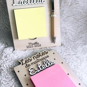 Può includere: Lavagne di legno con il testo "Les petites notes de maîtresse" e nomi personalizzati. Una lavagna ha un post-it giallo e il nome "Laetitia", l'altra ha un post-it rosa e il nome "Estelle". Una penna è attaccata alla prima lavagna.