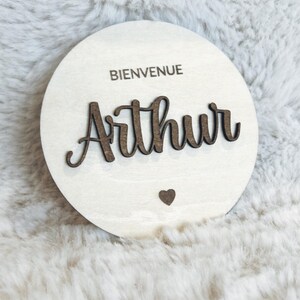 May include: A round wooden sign with the text "Bienvenue" and the name "Arthur" in cursive script. A small heart is below the name.