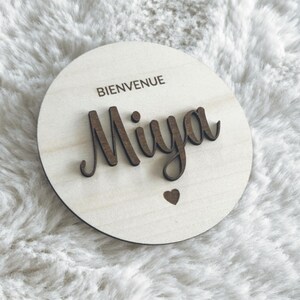 May include: A round wooden sign with the text "Bienvenue Miya" in cursive lettering and a small heart cutout.